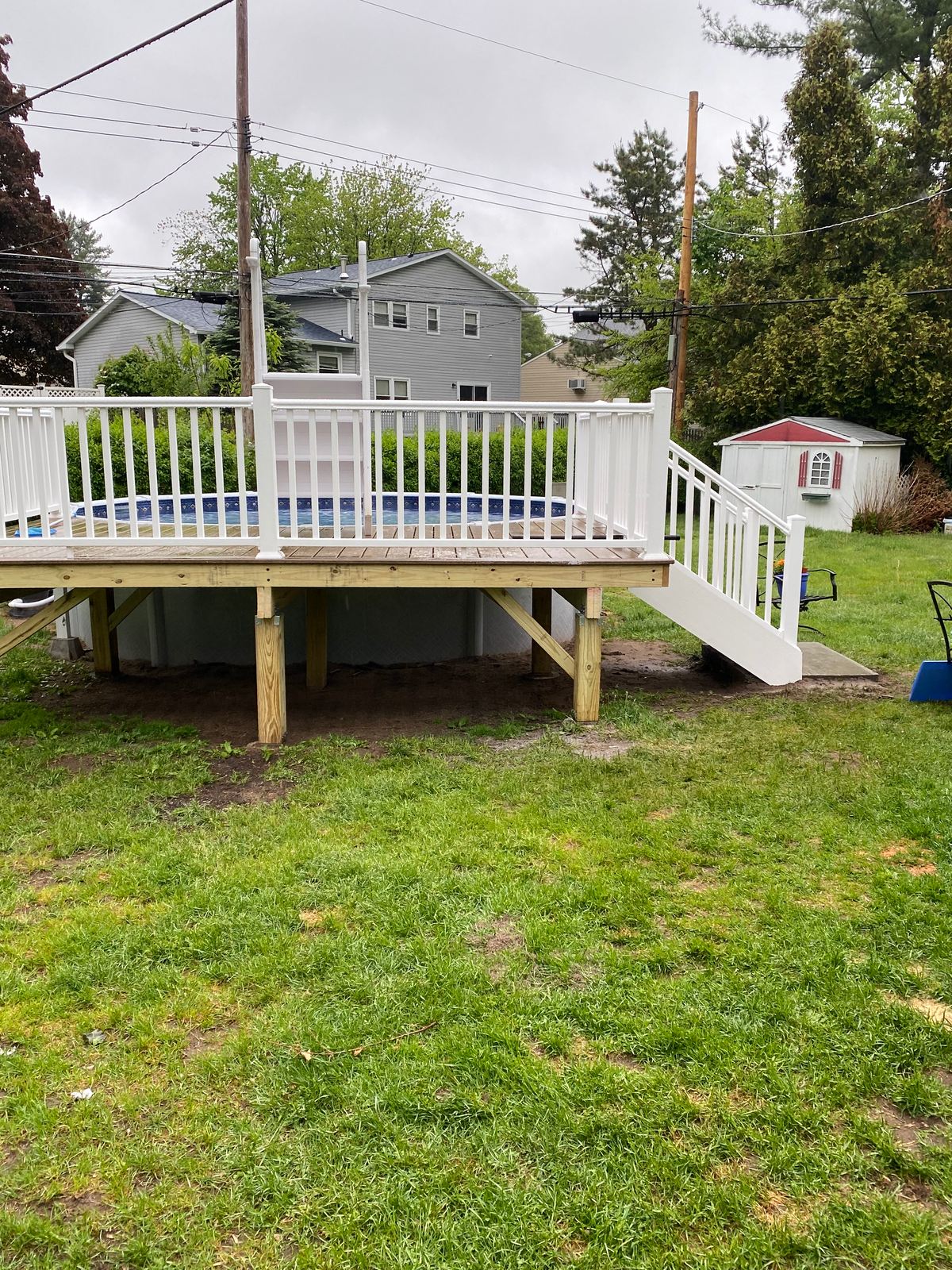 Raised deck beside an above-ground pool, with white railings and stairs