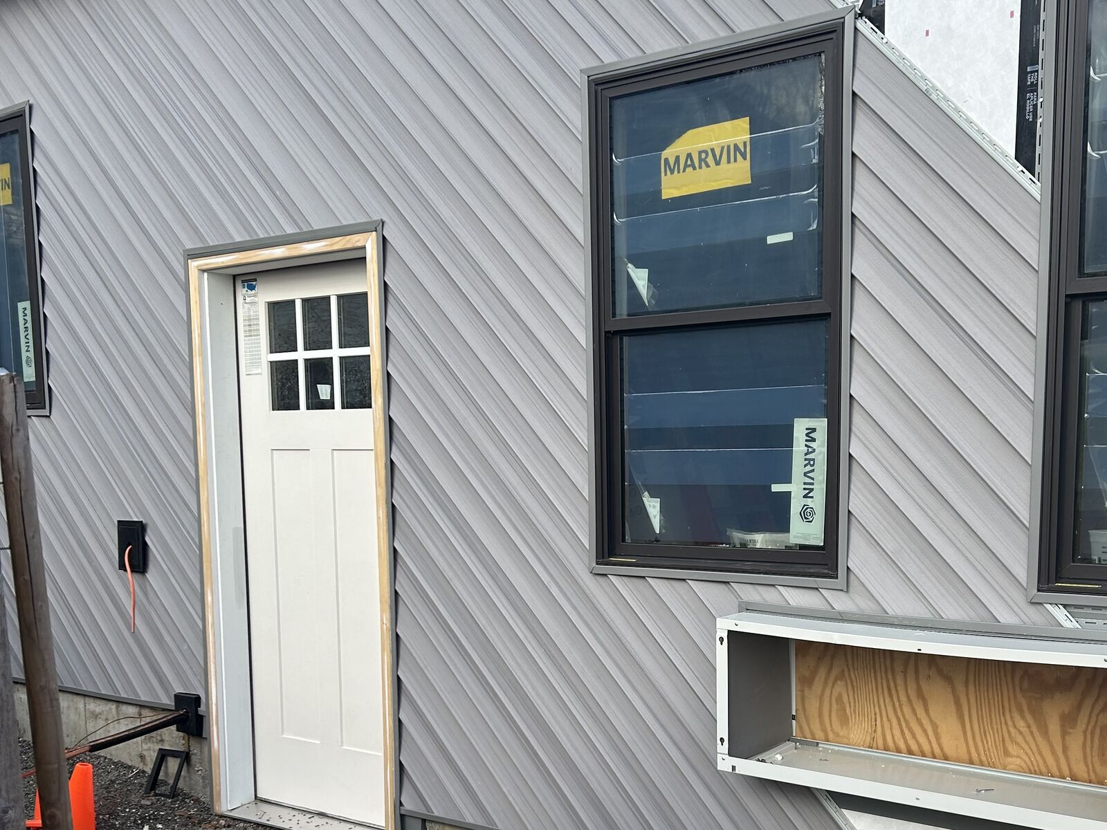 Diagonal gray siding going on over house wrap, with new windows and the entry door set